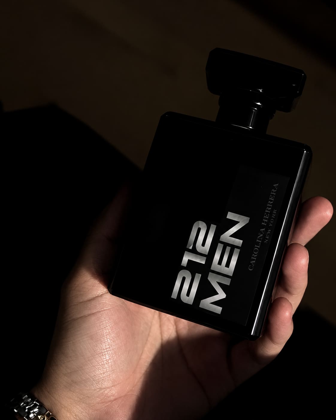 Mão segurando um frasco de perfume masculino sobre fundo escuro